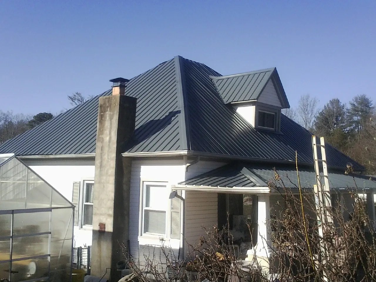 Dark blue standing seam metal roof on a white farmhouse with dormer — Slate & Tile Roof Repair by Roofing Brothers in Appalachia