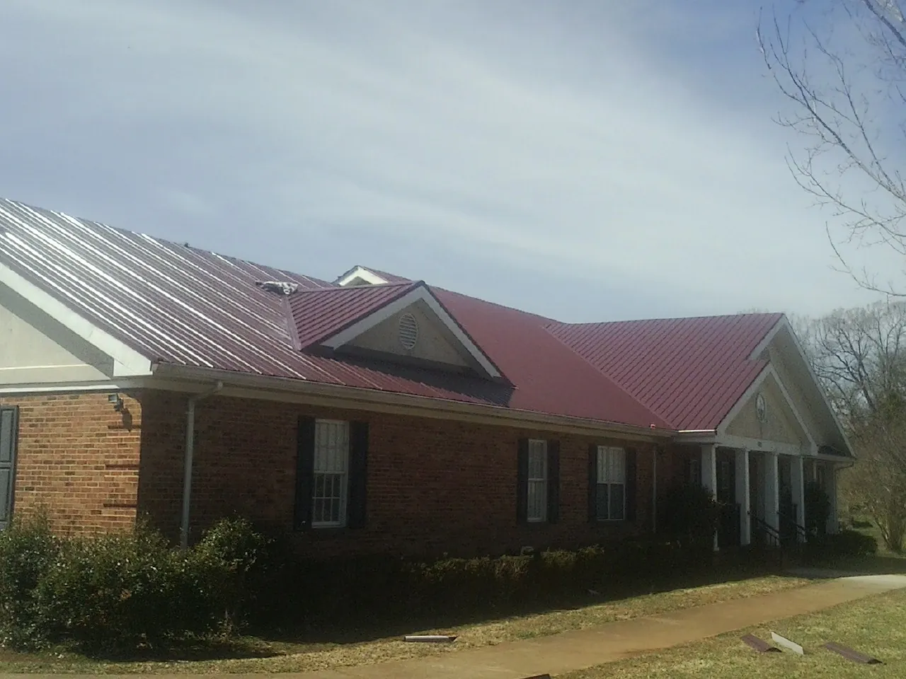 Red metal roof with gabled entries on a long brick building, from a Hail Damage Roof Repair job in Appalachia