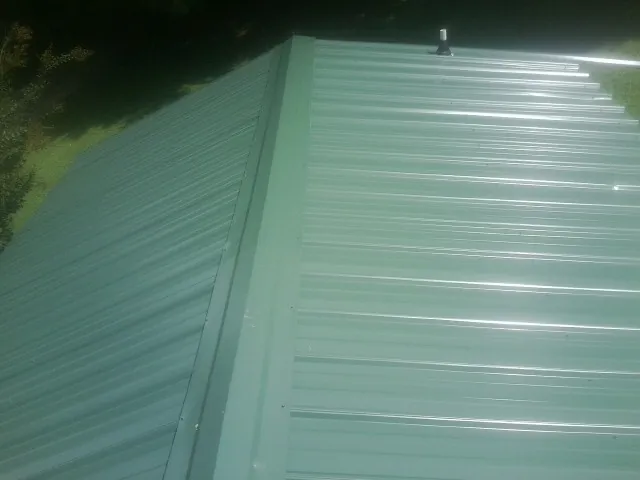 New green metal panels meeting at the ridge of a roof — Flat Roof Repair work by our crew in Appalachia
