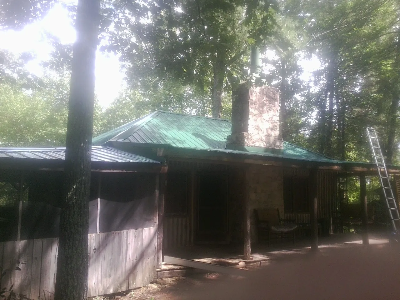 Green metal roof and stone chimney above a log cabin porch in Appalachia