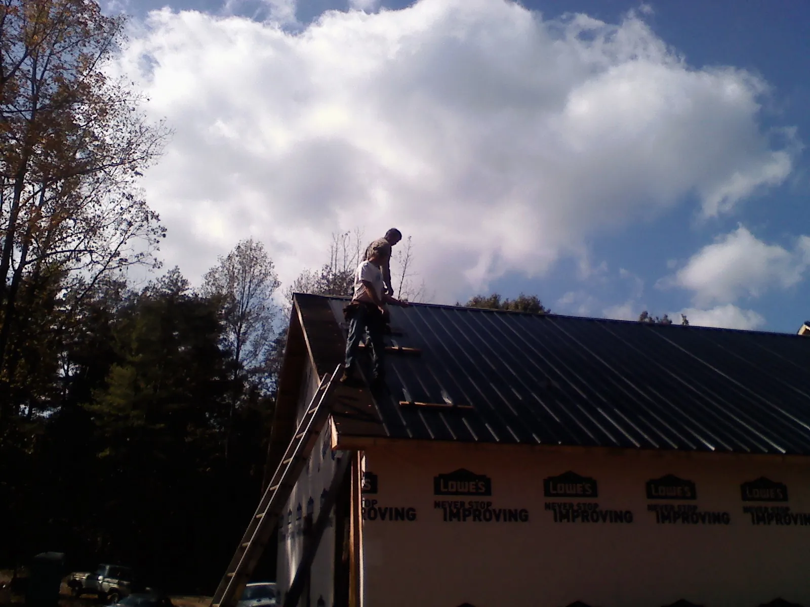 Roofer fastening dark metal panels high against a cloudy sky, from a Roof Inspection job in Appalachia