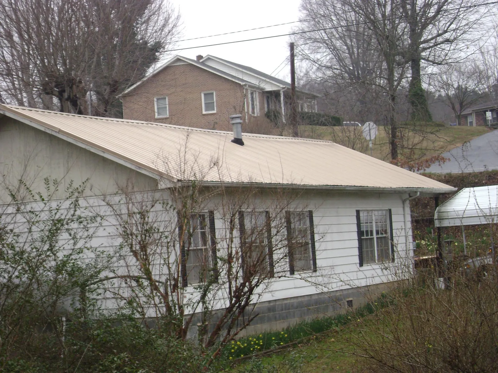 Tan metal roof on a white sided house set into a hillside — Commercial Roofing by Roofing Brothers in Appalachia