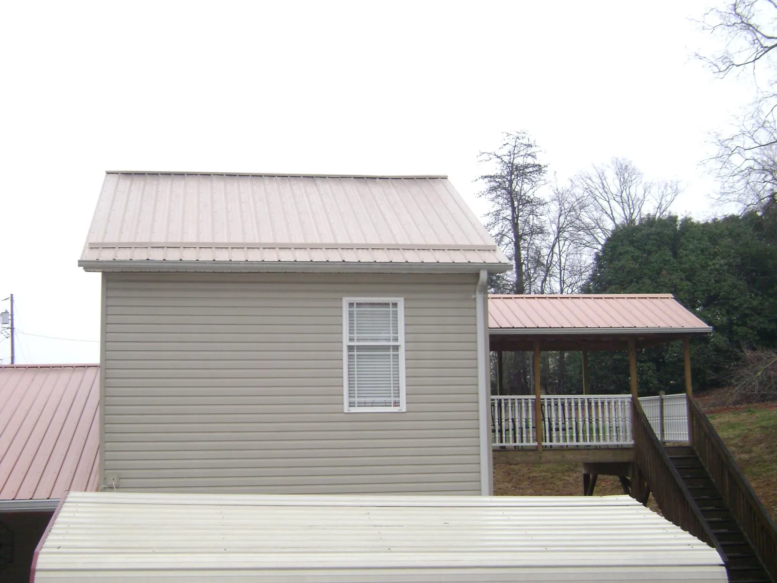 Tan metal roofs on a two story addition and attached porch, from a Roof Replacement job in Appalachia